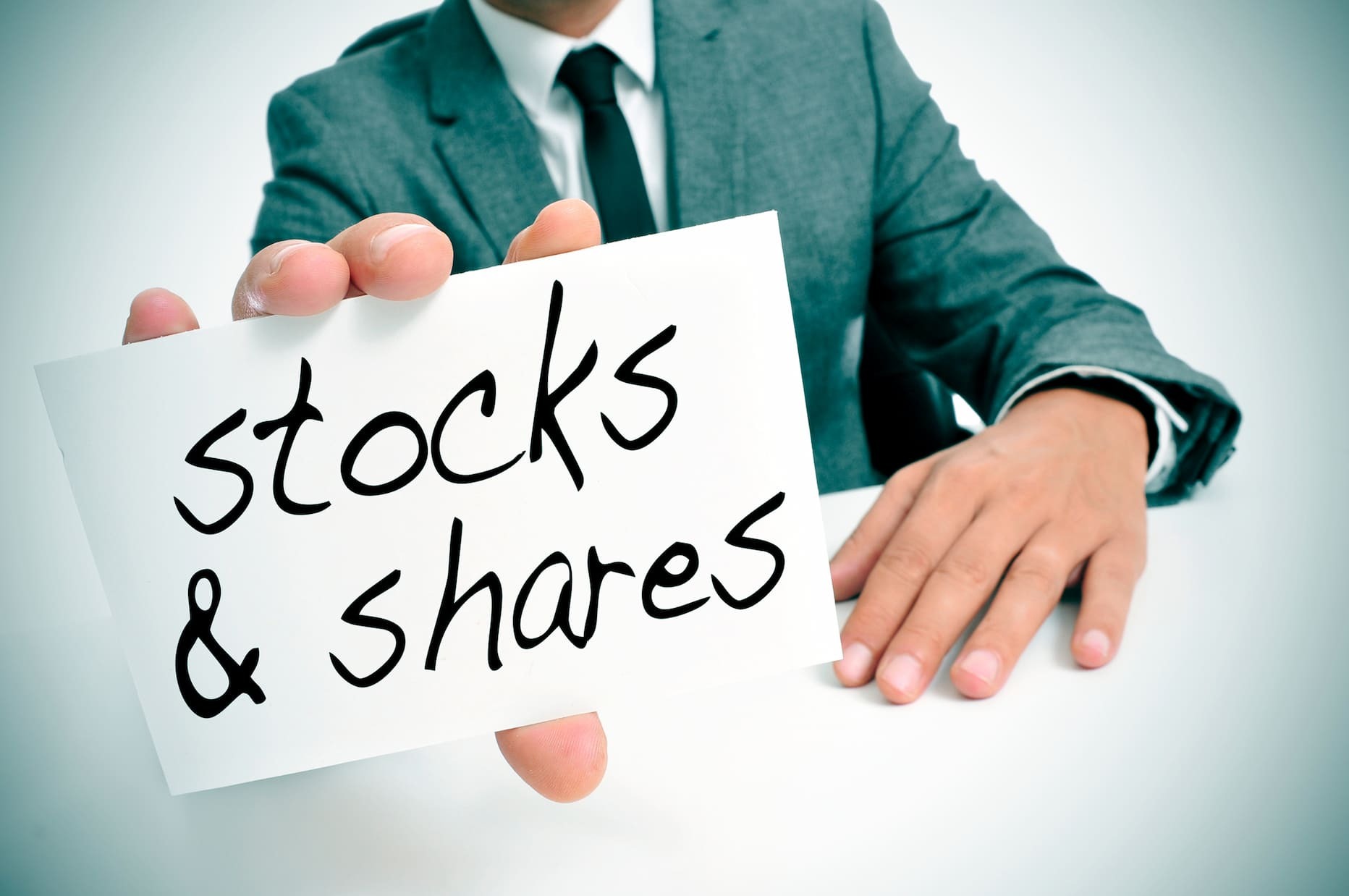 Man holding sign reading “stocks and shares,” representing investing, financial markets, and equity-based business growth concepts